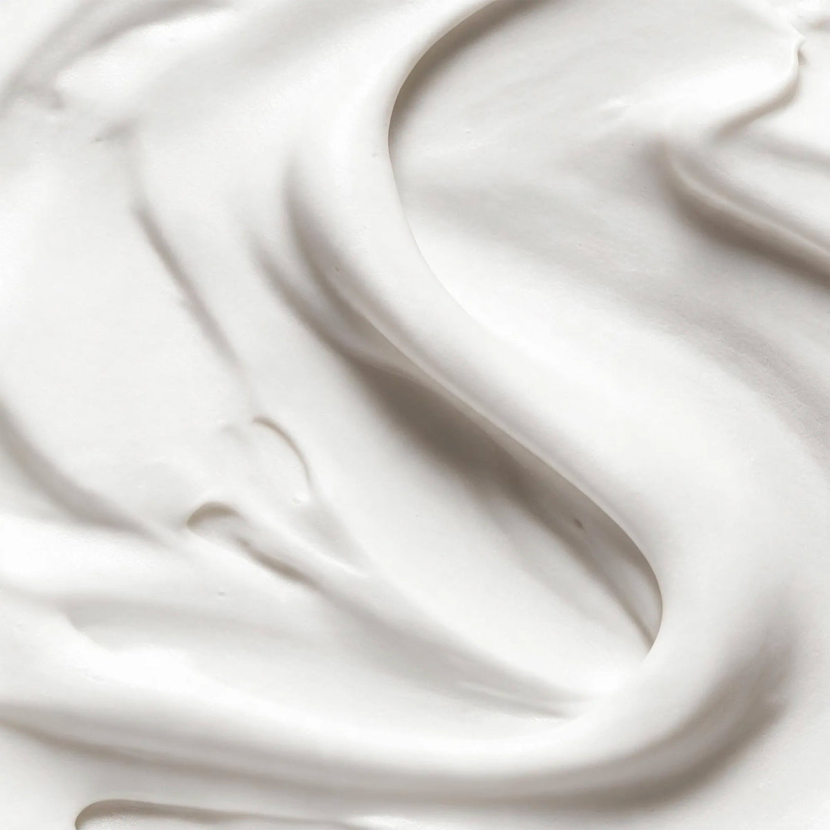 A close-up texture shot of thick, creamy white cosmetic cream with smooth, flowing swirls and soft shadows.