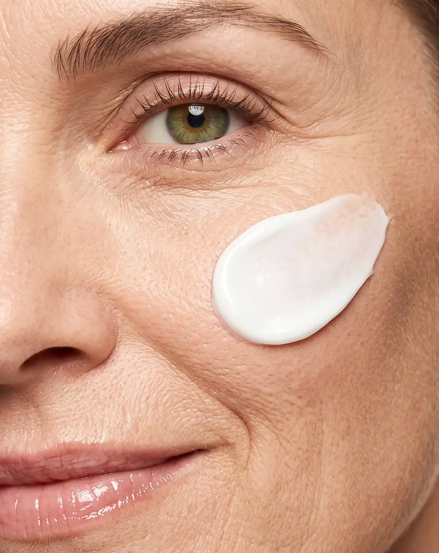 Close-up of a woman's face with a dollop of white cream applied to her cheek. [AI]