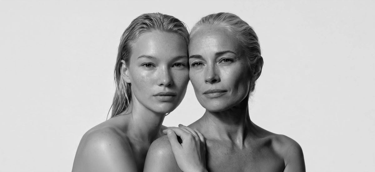 A black and white studio portrait of two women with wet, glistening skin posing closely together against a plain light background. [AI]