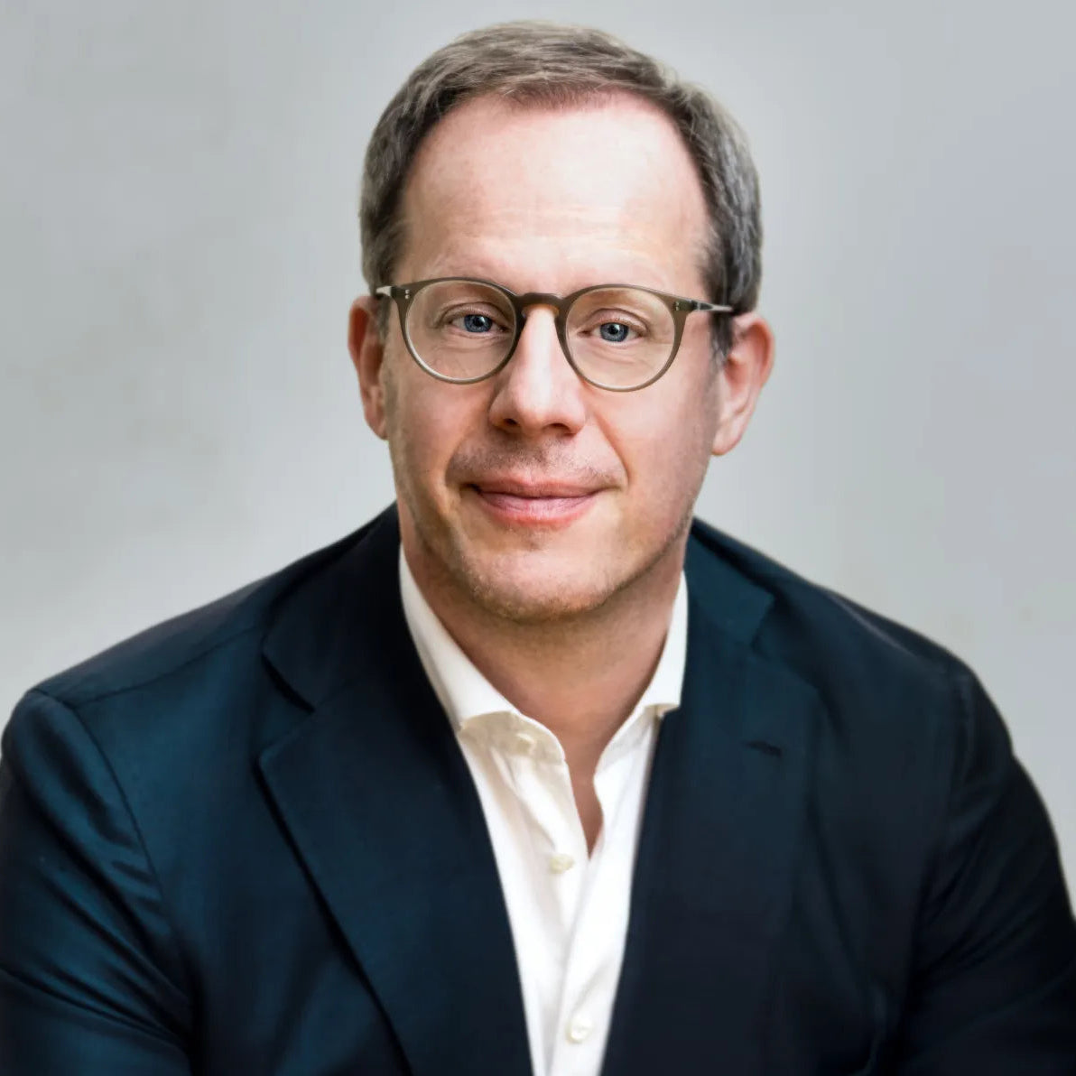 Stefan Kalmund wearing glasses and a dark suit on a gray background