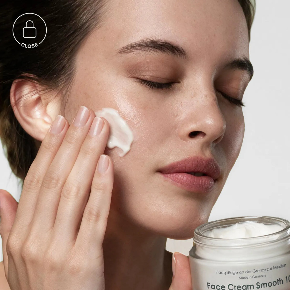 A close-up of a woman applying white face cream from a glass jar onto her cheek, with the jar labeled 'Face Cream Smooth 10' visible in the lower right corner. [AI]